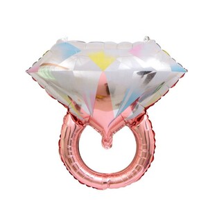 May include: A rose gold foil ring balloon with a large diamond-shaped balloon on top. The diamond balloon has a silver and iridescent finish with colorful accents.