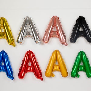 May include: A set of eight letter A balloons in different colors, including gold, silver, rose gold, black, blue, red, yellow, and green.