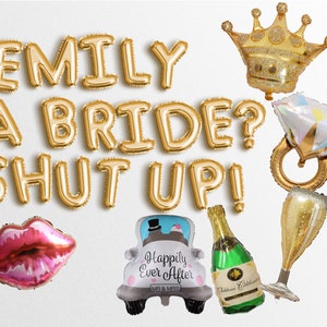 May include: Gold foil balloons spelling "EMILY A BRIDE? SHUT UP!" with additional balloons shaped like a crown, diamond ring, lips, a car with "Happily Ever After" text, champagne bottle, and a champagne flute. Perfect for a bachelorette party.