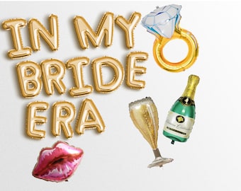 May include: Gold foil balloons spelling "In My Bride Era" with a pink lips balloon, a champagne flute balloon, a champagne bottle balloon, and a gold ring balloon with a white diamond.