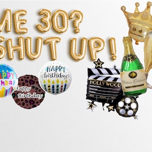 May include: Gold foil balloons spelling "ME 30? SHUT UP!" with a gold crown, champagne bottle, and champagne flute balloon. There are also three birthday balloons with the words "Happy Birthday" and a black and white clapperboard with the word "HOLLYWOOD" on it.