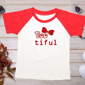 May include: White and red raglan t-shirt with a red bow and the text "Boo tiful" printed on the front.