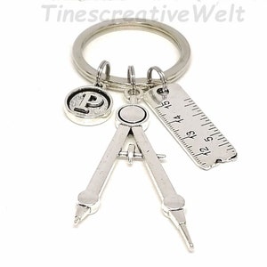 May include: Silver keychain with a compass charm, a ruler charm, and a charm with the letter P. The ruler has markings from 12 to 15.