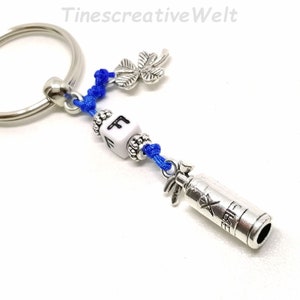 May include: A silver key chain with a blue cord, a silver charm of a fire extinguisher with the word "Fire" on it, a silver charm of a four-leaf clover, and a white cube charm with the letter "F" on it.