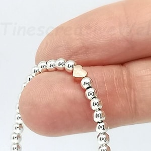 Könnte beinhalten: Ein silbernes Armband mit Perlen und einem goldenen Herz-Anhänger.