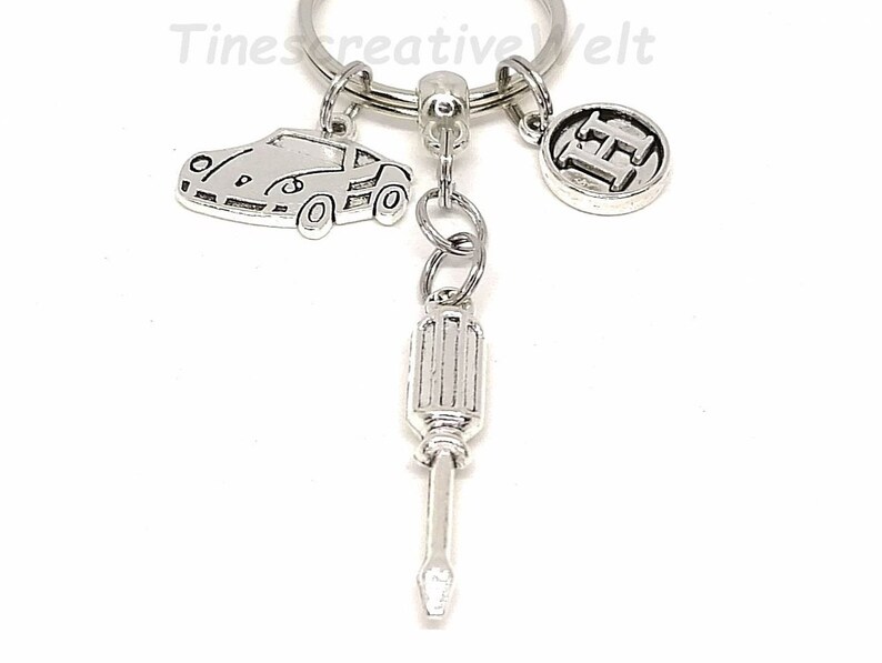 K&ouml;nnte beinhalten: Silberner Schl&uuml;sselanh&auml;nger mit einem Auto, einem Schraubendreher und einem Anh&auml;nger mit dem Buchstaben H.