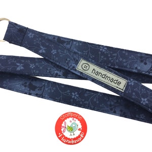 Könnte beinhalten: Ein blaues Stoffband mit weißem Blumenmuster und einem silbernen Ring. Das Band hat ein Etikett mit der Aufschrift "handgefertigt".