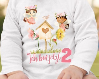 Könnte beinhalten: Weißes Langarmshirt mit farbenfroher Grafik. Das Design zeigt zwei Feen, ein Vogelhaus, Blumen und die Zahl 2 in Pink. Der Text "Ich bin jetzt" ist ebenfalls enthalten.