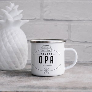 Könnte beinhalten: Weiße Emaille-Campingtasse mit schwarzem Umriss eines Campingbusses und dem Text "CAMPER OPA" in Schwarz. Der Text "DIE LIEBENSOHFT" ist ebenfalls in Schwarz unter dem Campingbus.