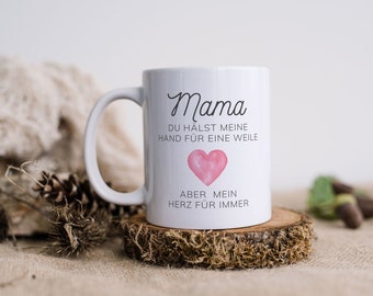 Könnte beinhalten: Weiße Keramiktasse mit einem schwarzen und rosafarbenen Design. Die Tasse trägt die Aufschrift "Mama du hältst meine Hand für eine Weile aber mein Herz für immer".