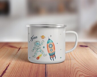 May include: White enamel mug with a blue and orange rocket and astronaut design. The mug has the name "Finn" written on it.