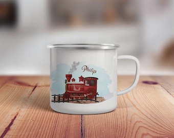 May include: White enamel mug with a red train illustration and the name Philip on a blue watercolor background.