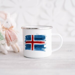 Könnte beinhalten: Weiße Emaille-Tasse mit einem blauen und roten Aquarell-Design der isländischen Flagge. Die Tasse hat einen silbernen Rand und einen Henkel.
