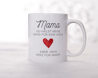 Könnte beinhalten: Weiße Keramiktasse mit einem schwarzen und roten Design. Die Tasse trägt die Aufschrift "Mama du hältst meine Hand für eine Weile aber mein Herz für immer" mit einem roten Herzen in der Mitte.