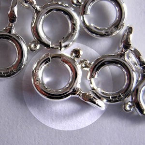 Könnte beinhalten: Nahaufnahme eines Stapels silberfarbener Metall-Sprühringe. Die Ringe haben einen Durchmesser von etwa 2,5 cm und einen federbelasteten Verschluss.