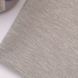 Puede incluir: Una pieza de tela gris claro con una textura finamente acanalada. El material muestra un patr&oacute;n de tejido consistente con l&iacute;neas verticales que recorren la superficie, creando una apariencia suave y uniforme en todo el tejido visible.