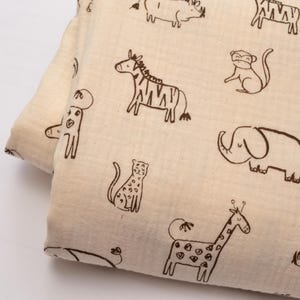 Puede incluir: Tela color crema con un patrón repetido de animales de safari en contornos marrones. Los animales incluyen una cebra, una jirafa, un elefante, un mono y un rinoceronte. La tela está doblada, mostrando el patrón en ambos lados.