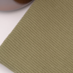 Puede incluir: Un trozo de tela de color verde oliva con una textura acanalada distintiva. El material muestra un patr&oacute;n vertical consistente de l&iacute;neas en relieve en toda su superficie, creando una apariencia uniforme y t&aacute;ctil en toda la secci&oacute;n visible del tejido.