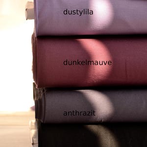 K&ouml;nnte beinhalten: Ein Stapel aus vier gefalteten Stoffballen in Unifarben. Der oberste Ballen ist mit 'dustylila' in hellem Violett beschriftet, gefolgt von 'dunkelmauve' in gedecktem Dunkelrosa, 'anthrazit' in Dunkelgrau und der unterste Ballen mit 'schwarz' in Schwarz.