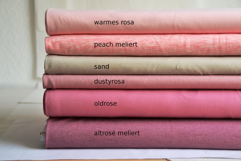 K&ouml;nnte beinhalten: Ein Stapel aus sechs gefalteten Stoffballen in verschiedenen Rosa-, Pfirsich- und Sandt&ouml;nen. Die Stofflagen sind mit folgendem Text beschriftet: warmes rosa, peach meliert, sand, dustyrosa, oldrose und altros&eacute; meliert, was die Farbe angibt.