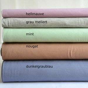 K&ouml;nnte beinhalten: Ein Stapel aus f&uuml;nf gefalteten Stoffballen in Unifarben. Die Farben von oben nach unten sind als hellmauve, grau meliert, mint, nougat und dunkelgraublau beschriftet. Jeder Stoffballen ist ordentlich horizontal &uuml;bereinander geschichtet.