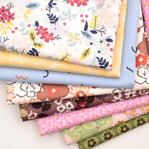 Könnte beinhalten: Ein Stapel verschiedener Stoffmuster mit Blumenmustern. Die Stoffe weisen eine Reihe von Farben auf, darunter Weiß, Gelb, Blau, Braun, Rosa und Grün. Die Muster umfassen Blumen, Blätter und geometrische Designs, geeignet für Näh- und Bastelprojekte.
