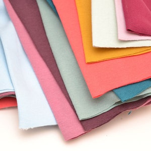 Könnte beinhalten: Ein Stapel Stoffmuster in verschiedenen Farben, darunter hellblau, rosa, türkis, orange und burgunderrot.