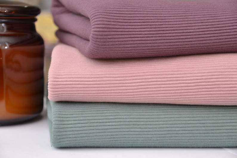 Puede incluir: Una pila de tres piezas de tela acanalada dobladas en colores s&oacute;lidos. La pieza superior es de un color malva profundo, la pieza central es de un rosa suave y la pieza inferior es de un verde salvia apagado. Cada capa presenta una textura acanalada vertical.