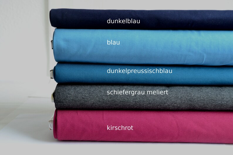 K&ouml;nnte beinhalten: Ein Stapel aus f&uuml;nf gefalteten Stoffballen in verschiedenen Farben. Die Farben von oben nach unten sind als dunkelblau, blau, dunkelpreussischblau, schiefergrau meliert und kirschrot beschriftet. Jeder Stoffballen ist ordentlich horizontal geschichtet.
