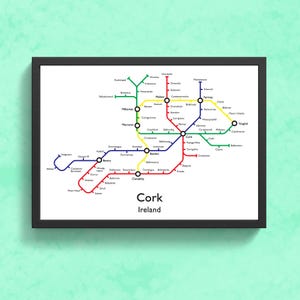May include: A framed print depicting a colourful schematic map of Cork, Ireland, styled like a subway map. The map uses coloured lines to represent routes, with station names in white. The print is presented in a black frame.