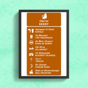 May include: A brown and white sign with the text "Ciarraí KERRY" at the top. The sign lists various locations in County Kerry, Ireland, with their Irish and English names. The locations include Dingle, The Maherees, Ring of Kerry, Killarney, Blasket Islands, Tralee, Conor Pass, and Ballybunion.
