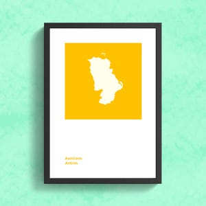 Puede incluir: Impresi&oacute;n art&iacute;stica enmarcada con un contorno blanco de una regi&oacute;n geogr&aacute;fica sobre un fondo amarillo. La impresi&oacute;n incluye el texto "Aontroim Antrim" en la parte inferior, todo dentro de un marco negro. La obra de arte se muestra contra una pared texturizada verde claro.