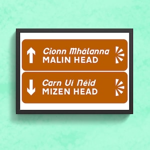 Puede incluir: Un letrero marrón y blanco con dos flechas direccionales. La flecha superior apunta hacia arriba y dice "Cionn Mhálánna MALIN HEAD". La flecha inferior apunta hacia abajo y dice "Carn Uí Néid MIZEN HEAD".