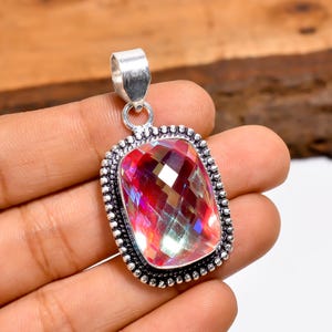 May include: A rectangular pendant featuring a large, faceted, iridescent gemstone. The gem displays shades of red, pink, and purple. It is set in a silver-coloured metal frame with a beaded border and a loop for a chain.