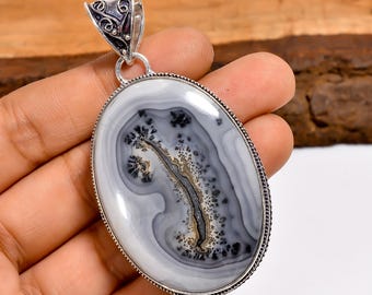 May include: Oval pendant with a polished, marbled stone in shades of gray, black, and brown, set in a silver-toned metal frame. The stone's pattern resembles a landscape. The pendant has a decorative bail.