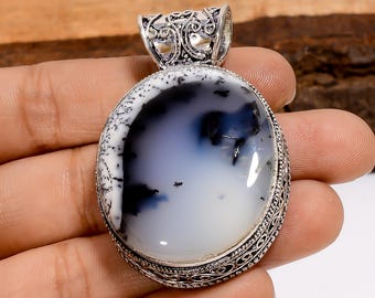 Pode incluir: Pingente oval com moldura prateada. O pingente apresenta uma pedra grande e polida com um padrão branco, preto e azul. A moldura tem um design ornamentado na parte superior e ao redor da borda da pedra.