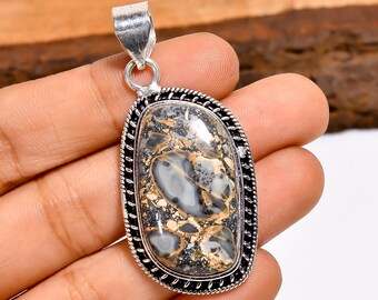 May include: A silver pendant with an oval, patterned stone. The stone features a mix of gray, black, and gold colors. The pendant has a decorative, twisted rope-like border and a silver bail for a chain.