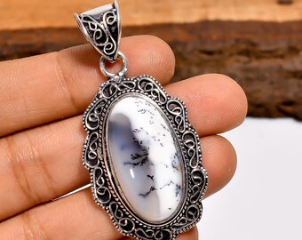 Pode incluir: Pingente oval com uma pedra de ágata dendrítica branca e preta emoldurada em uma moldura decorativa de metal prateado. O pingente tem uma argola ornamentada para prender a uma corrente.