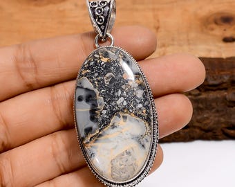 May include: Oval pendant with a silver bail and a natural stone. The stone features a mix of black, gray, and cream colors with a unique pattern. The pendant is likely a piece of jewelry.