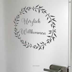 May include: A grey vinyl decal with a wreath of leaves and the text "Herzlich Willkommen" in a cursive font.