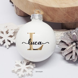 Könnte beinhalten: Weißer Weihnachtsbaumschmuck mit einem goldenen Buchstaben L und dem Namen "luca" in schwarzer Schreibschrift.