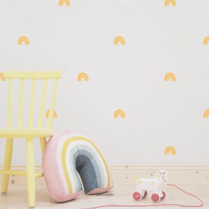 Puede incluir: Una pared blanca con calcoman&iacute;as de arco&iacute;ris amarillas. Una silla amarilla con una almohada de arco&iacute;ris se encuentra frente a la pared. Un caballo de juguete blanco con ruedas rojas est&aacute; en el suelo.