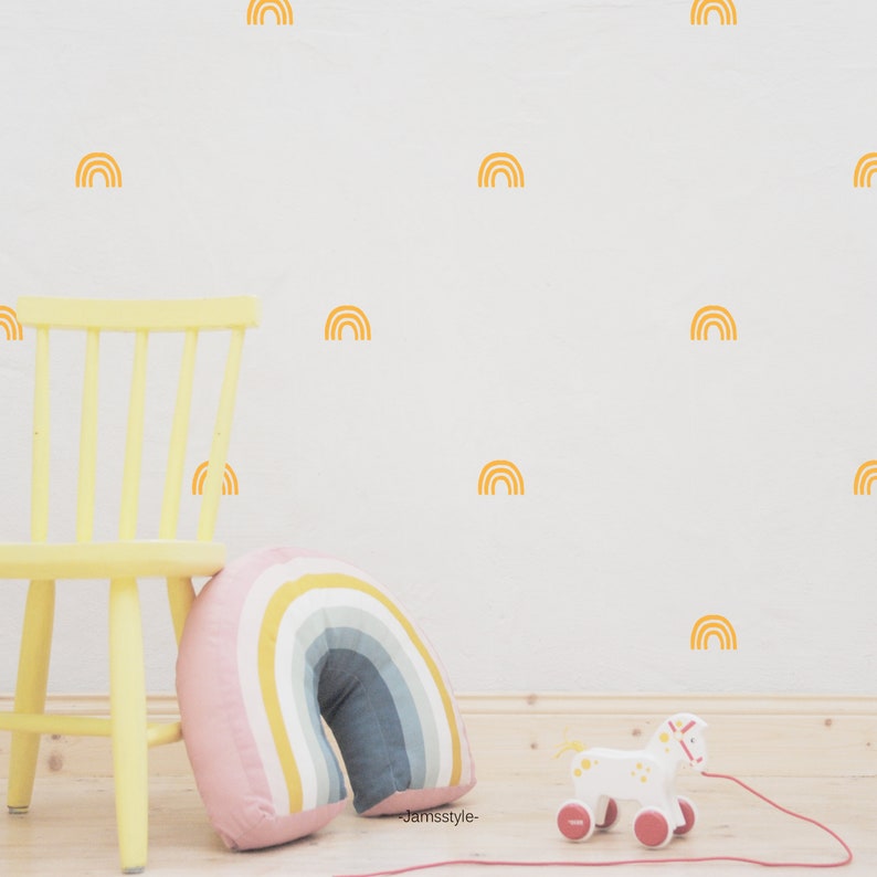 Puede incluir: Una pared blanca con calcoman&iacute;as de arco&iacute;ris amarillas. Una silla amarilla con una almohada de arco&iacute;ris se encuentra frente a la pared. Un caballo de juguete blanco con ruedas rojas est&aacute; en el suelo.