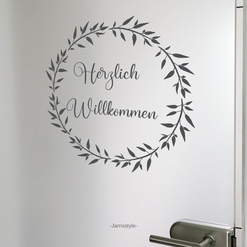 May include: A grey vinyl decal with a wreath of leaves and the text "Herzlich Willkommen" in a cursive font.