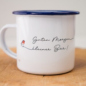 May include: White enamel mug with a blue rim and a robin illustration. The mug has the text "Guten Morgen kleiner B&auml;r!" printed on it.