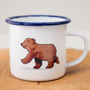May include: White enamel mug with a blue rim featuring a brown bear illustration.