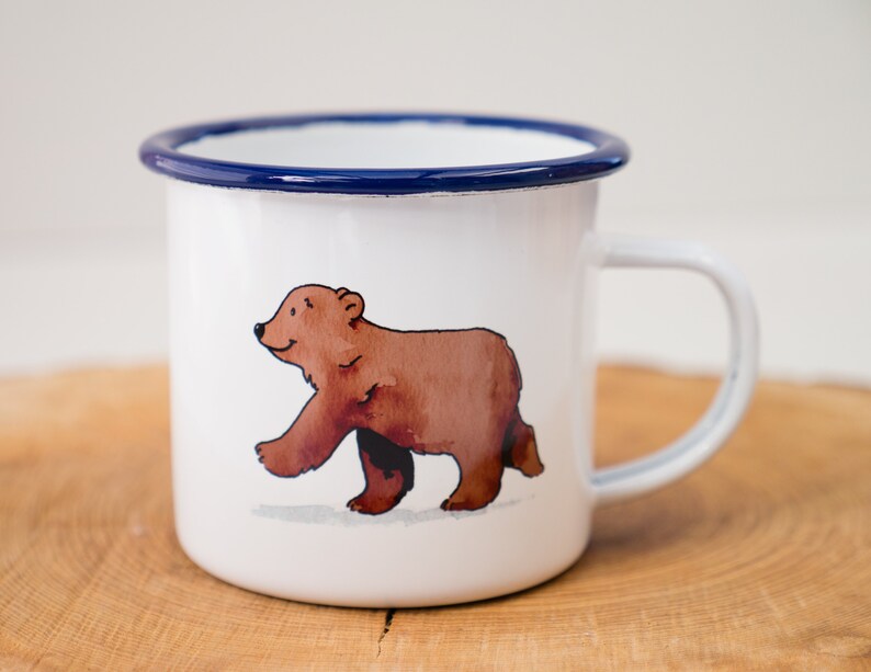 May include: White enamel mug with a blue rim featuring a brown bear illustration.