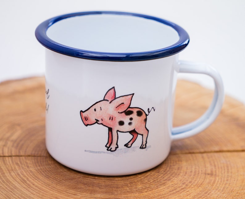 May include: White enamel mug with a blue rim and a hand-painted illustration of a pink pig with black spots. The pig is looking to the left and has a curly tail.