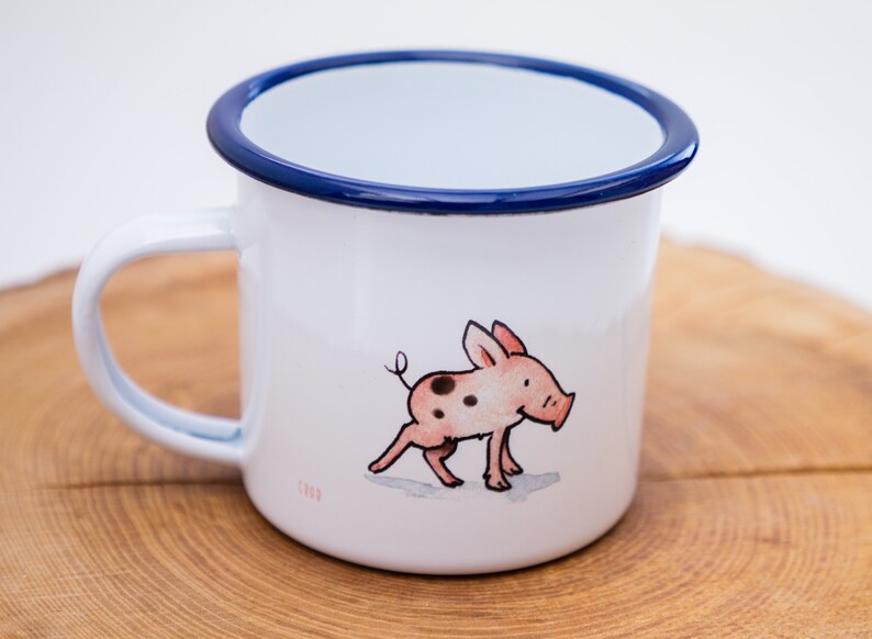May include: White enamel mug with a blue rim and a hand-drawn illustration of a pink pig with black spots.