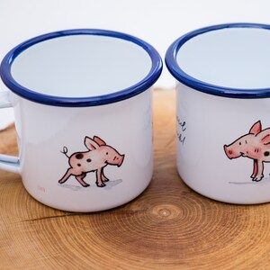 May include: Two white enamel mugs with blue rims. Each mug features a cartoon illustration of a pink pig with black spots. One mug has the text "You are my sunshine" on it.